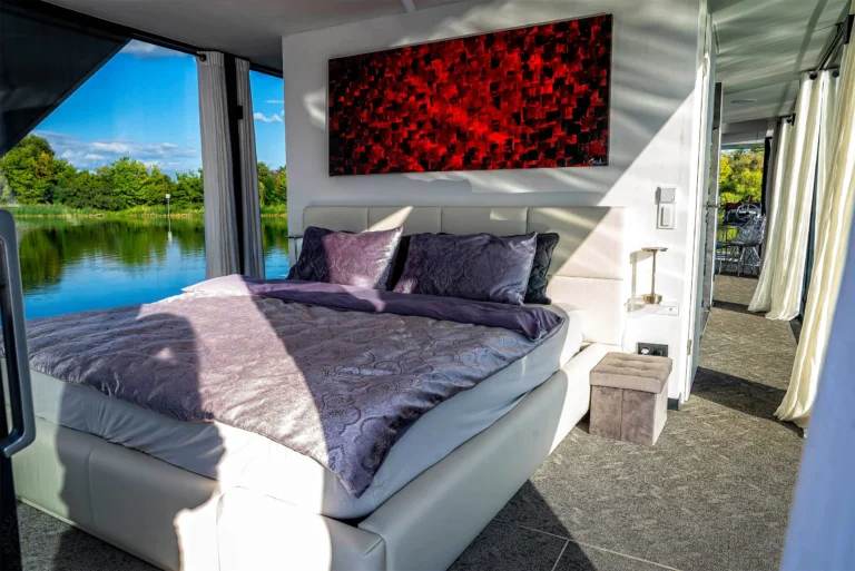 Helles Schlafzimmer im Hausboot mit Doppelbett und Panoramablick auf den See