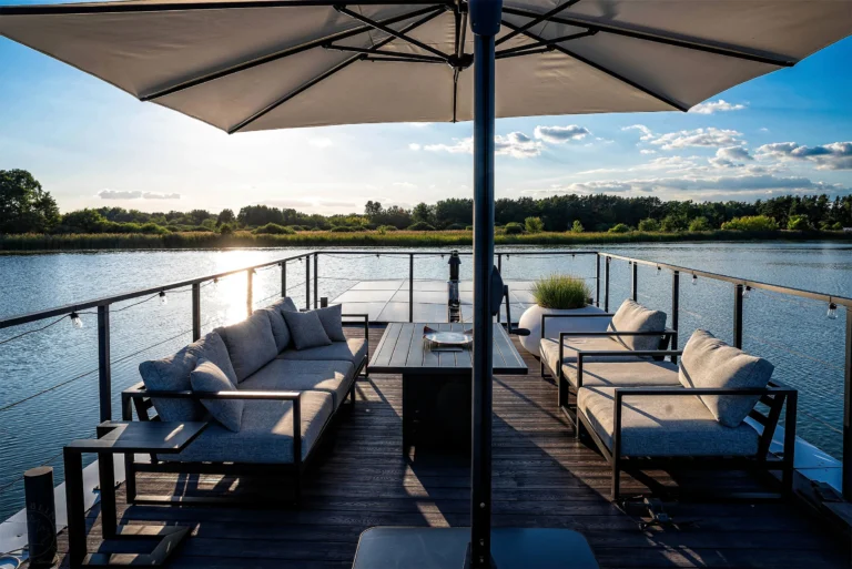 Dachterrasse mit Lounge-Sitzgruppe und Sonnenschirm im Gegenlicht über dem See