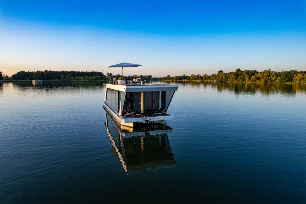 Luxus-Hausboot allein auf einem ruhigen Havelsee im Morgenlicht, umgeben von Wald und Schilf