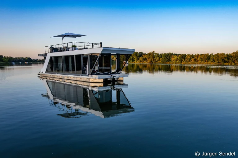 Hausboot mit Dachterrasse auf spiegelglattem See im Abendlicht
