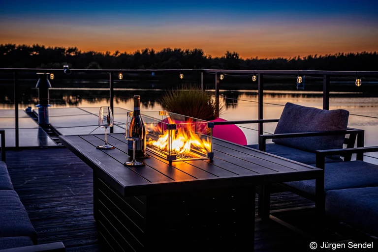 Feuertisch mit Champagner auf der Terrasse bei Sonnenuntergang am See