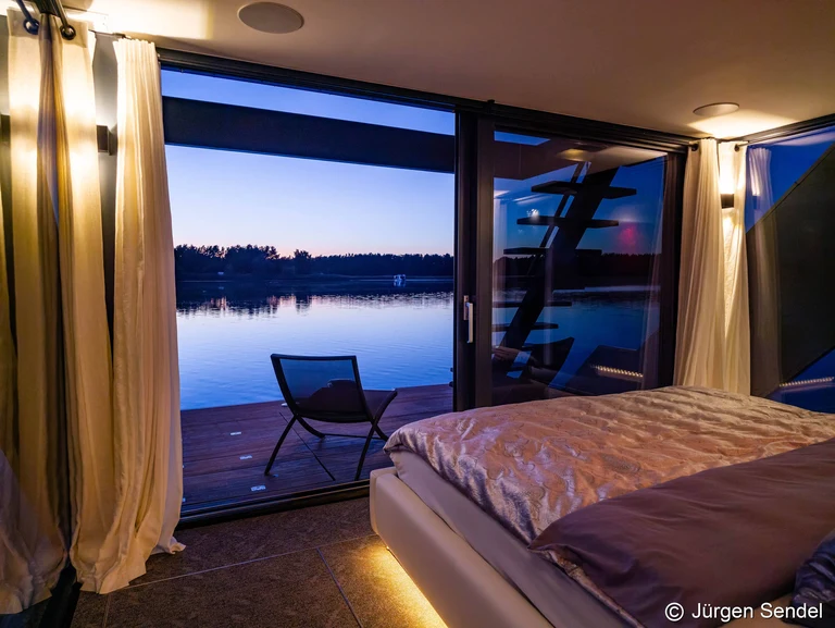 Blick aus dem Schlafzimmer durch die offene Schiebetür auf den See in der Dämmerung