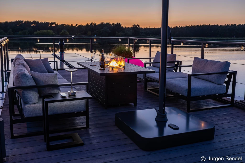 Terrasse am Abend mit Feuertisch und Lounge-Möbeln über dem Wasser