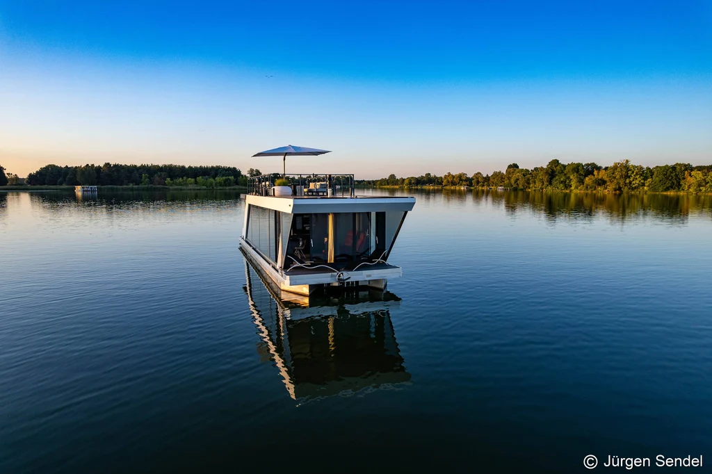 Luxus-Hausboot allein auf einem ruhigen Havelsee im Morgenlicht, umgeben von Wald und Schilf